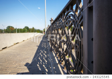 Geometric shadows cast from ornate metal fence on paved city bridge walkway in bright sunlight with copy space 143125545