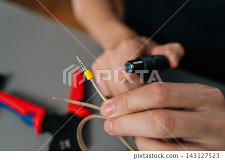 Technician hands heat shrinking electrical cable with torch lighter, insulating and repairing wiring connections with precision during maintenance work in workshop setting, close-up, cropped shot Technician hands heat shrinking electrical cable with torch lighter, insulating and repairing wiring connections with precision during maintenance work in workshop setting, close-up, cropped shot 143127523