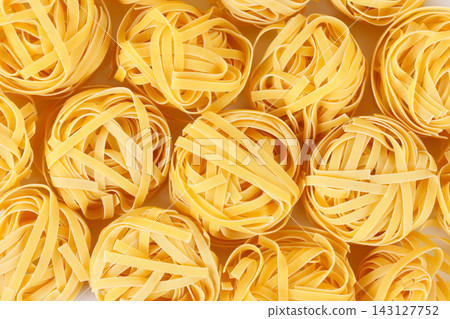 Textured culinary background featuring raw tagliatelle nests coiled and yellow hued. Textured culinary background featuring raw tagliatelle nests coiled and yellow hued. 143127752