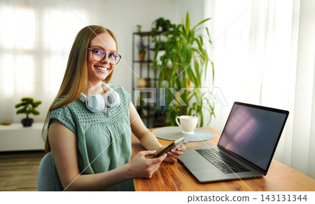 Young woman smiling working from home using technology Young woman smiling working from home using technology 143131344