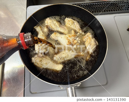 A salaryman makes chicken wings braised in cola in a frying pan after work. A salaryman makes chicken wings braised in cola in a frying pan after work. 143131390