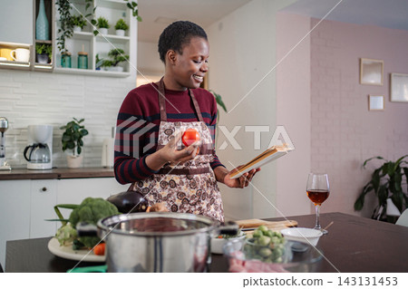 Woman cooking healthy fresh meal using kitchen recipe book Woman cooking healthy fresh meal using kitchen recipe book 143131453
