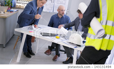 Briefing at the construction company. Meeting of the foreman, architect and engineers. A group of people is sitting at a table with drawings and papers Briefing at the construction company. Meeting of the foreman, architect and engineers. A group of people is sitting at a table with drawings and papers 143131494