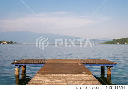 Wooden pier extending into a calm lake with mountain backdrop 143131864