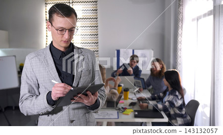 Working as a personal assistant in a large company. A handsome, focused man in a suit and glasses is writing on a tablet Working as a personal assistant in a large company. A handsome, focused man in a suit and glasses is writing on a tablet 143132057