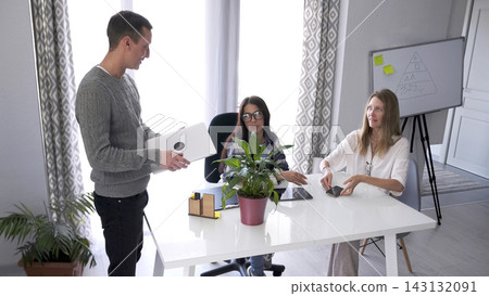 A young man with a laptop entered the office of the Director of public relations. Two beautiful women are sitting at a table A young man with a laptop entered the office of the Director of public relations. Two beautiful women are sitting at a table 143132091