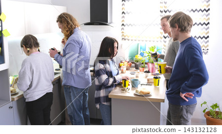 A group of young entrepreneurs organized a coffee break in the office kitchen of the family office. The staff is gathered around the kitchen table A group of young entrepreneurs organized a coffee break in the office kitchen of the family office. The staff is gathered around the kitchen table 143132128