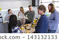 Company employees have lunch and drink coffee in the office kitchen. A group of people gathers around a kitchen island for a conversation 143132133