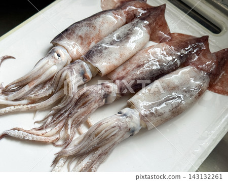 A food photograph showing fresh squid arranged in white on a cutting board before cooking. A food photograph showing fresh squid arranged in white on a cutting board before cooking. 143132261