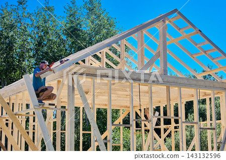 Rafters are secured within timber framework, construction worker uses compact level to ensure precise alignment. 143132596