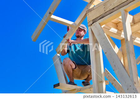 Rafters are positioned within timber framework, construction worker uses compact level to confirm alignment accuracy. Rafters are positioned within timber framework, construction worker uses compact level to confirm alignment accuracy. 143132613