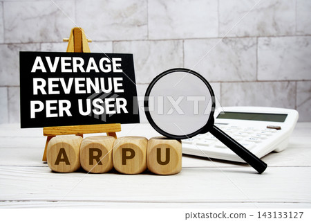 ARPU Average Revenue Per User text with calculator magnifying glass and on wooden background 143133127