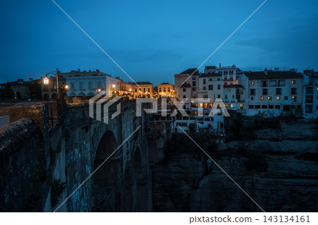 Stone arches of Puente Nuevo and cliffside houses above the gorge at blue hour in Ronda Stone arches of Puente Nuevo and cliffside houses above the gorge at blue hour in Ronda 143134161
