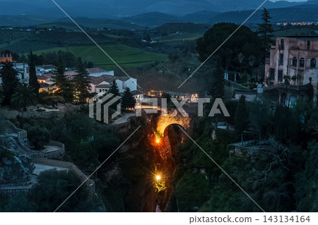 Illuminated bridge deep in the Tajo gorge at blue hour with birds flying over Ronda Illuminated bridge deep in the Tajo gorge at blue hour with birds flying over Ronda 143134164