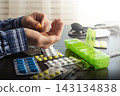 Middle aged caucasian man counts out pills for distributing scheduled dose of medication into pillbox 143134838