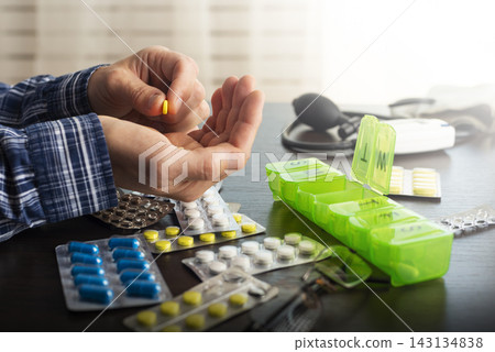Middle aged caucasian man counts out pills for distributing scheduled dose of medication into pillbox Middle aged caucasian man counts out pills for distributing scheduled dose of medication into pillbox 143134838