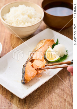 A traditional Japanese breakfast at home, where you pick up grilled salmon with chopsticks and enjoy it with white rice. A traditional Japanese breakfast at home, where you pick up grilled salmon with chopsticks and enjoy it with white rice. 143136871