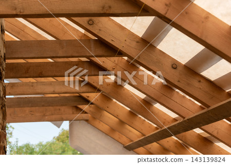 Wooden roof rafters and beams forming the framed structure of a new residential house, showcasing carpentry, timber framing and the unfinished construction process and craftsmanship Wooden roof rafters and beams forming the framed structure of a new residential house, showcasing carpentry, timber framing and the unfinished construction process and craftsmanship 143139824