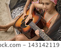 A girl plays the guitar sitting in a tent. 143142119