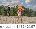 The girl helps her dad launch a rainbow kite into the sky. 143142167