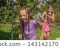 A close up of a wet, laughing girl running away from a stream of water.  143142170
