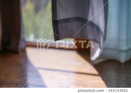 陽光透過樹葉灑落在木地板和蕾絲窗簾上，宛如陽光穿透樹葉的斑駁光影。 143143082