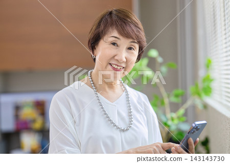 一位六十多歲的女士在辦公室裡看著她的智慧型手機。 一位六十多歲的女士在辦公室裡看著她的智慧型手機。 143143730