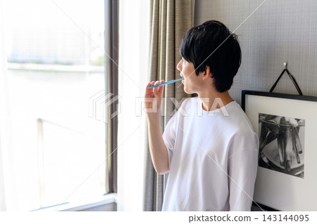 一名男子在窗邊用牙刷刷牙。 一名男子在窗邊用牙刷刷牙。 143144095