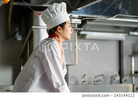 A female chef touches her neck while taking a break in the kitchen. A female chef touches her neck while taking a break in the kitchen. 143144122
