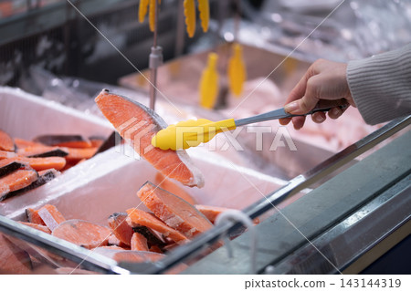 顧客用夾子在超市鮮魚區挑選鮭魚片。 顧客用夾子在超市鮮魚區挑選鮭魚片。 143144319