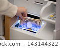 A woman's hands as she deposits and withdraws a 10,000 yen bill (new banknote) at a bank or convenience store ATM. 143144322