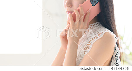 一位女士一邊用智慧型手機通話，一邊側臉示意。 143144806