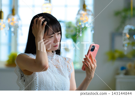 一位年輕的日本女子憂心忡忡地看著她的智慧型手機。 一位年輕的日本女子憂心忡忡地看著她的智慧型手機。 143144844