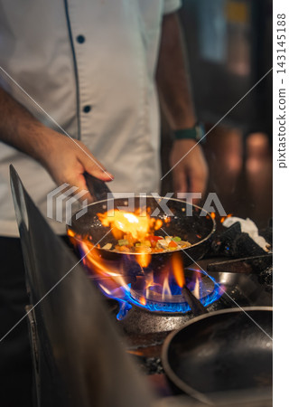 Chef sautes vegetables over gas flame in Maldives hotel kitchen Chef sautes vegetables over gas flame in Maldives hotel kitchen 143145188