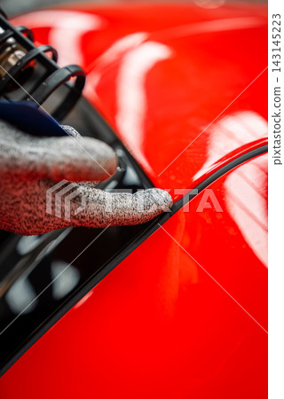 Technician aligns panel gap and trim on glossy red luxury car Technician aligns panel gap and trim on glossy red luxury car 143145223