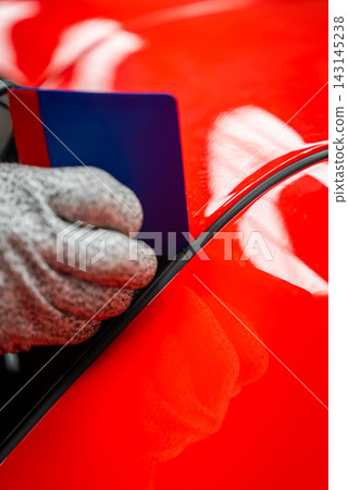 Gloved technician applies trim with squeegee on glossy red car panel Gloved technician applies trim with squeegee on glossy red car panel 143145238