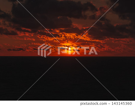 Solar eclipse during sunset over ocean with dark clouds 143145360