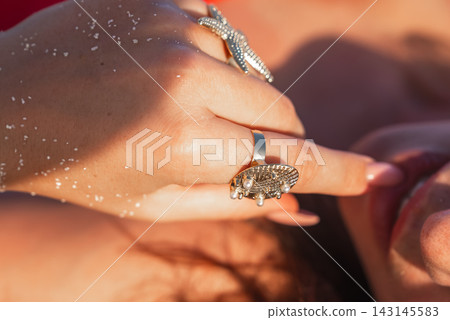 A woman wearing golden rings touches her face while lying on the beach A woman wearing golden rings touches her face while lying on the beach 143145583