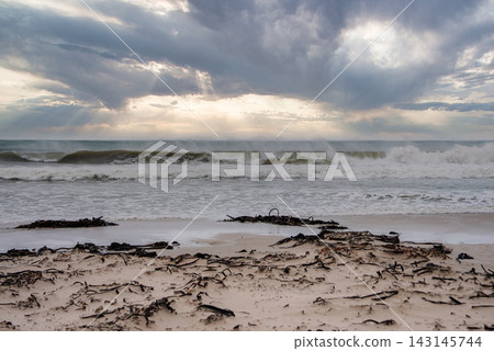 Ocean waves crash on a sandy beach under stormy clouds in Cape Town 143145744