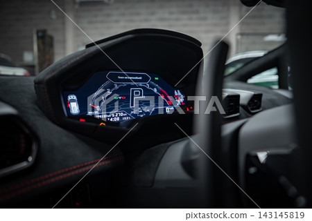 Close up shows a Lamborghini Huracan digital cluster in Park, with central P, gauges, nav graphics, Alcantara trim, red stitching, hex vents, in an indoor showroom. Close up shows a Lamborghini Huracan digital cluster in Park, with central P, gauges, nav graphics, Alcantara trim, red stitching, hex vents, in an indoor showroom. 143145819