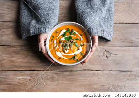 Bowl of pumpkin soup in woman hands Bowl of pumpkin soup in woman hands 143145950