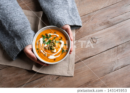 Female hands in knitted sweater holding bowl with pumpkin soup Female hands in knitted sweater holding bowl with pumpkin soup 143145953