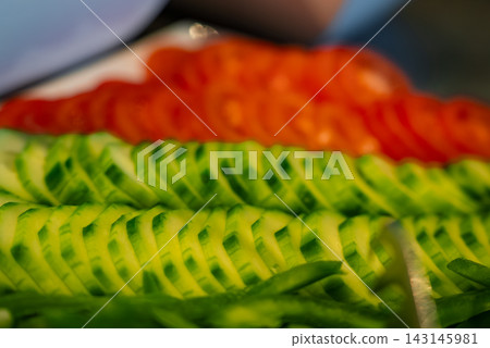 Neat rows of thin cucumber and tomato slices fill the frame in Oberlech, Austria. Soft indoor lighting and shallow depth of field suggest a kitchen prep station. Neat rows of thin cucumber and tomato slices fill the frame in Oberlech, Austria. Soft indoor lighting and shallow depth of field suggest a kitchen prep station. 143145981