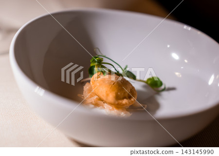 A golden fried dumpling rests on pickled vegetables and microgreens in a deep white bowl, warm focused lighting and shallow depth of field suggest fine dining in the Dolomites. A golden fried dumpling rests on pickled vegetables and microgreens in a deep white bowl, warm focused lighting and shallow depth of field suggest fine dining in the Dolomites. 143145990