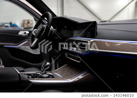 Interior view of a white BMW X7 shows cockpit and center console, crystal gear selector, iDrive controller, widescreen display, hexagonal vents, and ambient LED lighting. Interior view of a white BMW X7 shows cockpit and center console, crystal gear selector, iDrive controller, widescreen display, hexagonal vents, and ambient LED lighting. 143146010