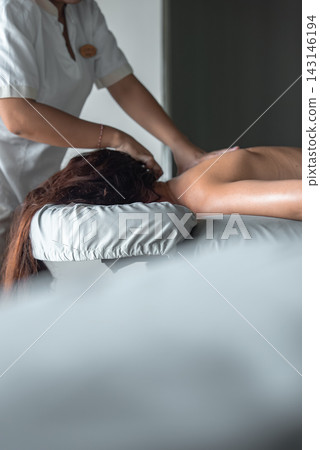 A spa therapist in a white uniform massages a guest on a padded table indoors. Soft diffused light and muted gray blue tones suggest a Maldives luxury spa setting. A spa therapist in a white uniform massages a guest on a padded table indoors. Soft diffused light and muted gray blue tones suggest a Maldives luxury spa setting. 143146194