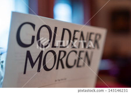 A close up shows the Goldener Morgen headline on a sheet in a luxury winter hotel in Oberlech, Austria. Warm indoor lighting and wooden interiors appear softly blurred. A close up shows the Goldener Morgen headline on a sheet in a luxury winter hotel in Oberlech, Austria. Warm indoor lighting and wooden interiors appear softly blurred. 143146231