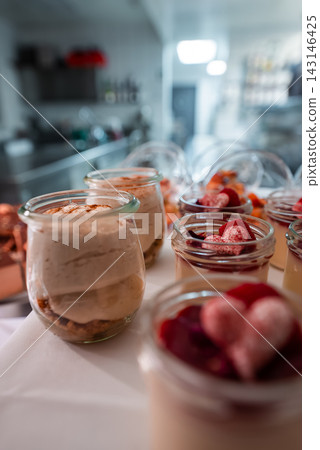 Close up dessert jars sit on a white tray in Oberlech, Austria. Layers of creamy mousse, biscuit crumb, raspberry coulis, and berries glisten under soft, cool light. Close up dessert jars sit on a white tray in Oberlech, Austria. Layers of creamy mousse, biscuit crumb, raspberry coulis, and berries glisten under soft, cool light. 143146425