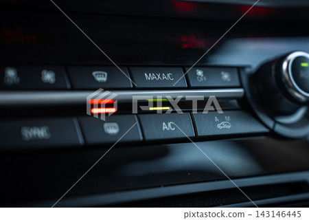 Close view of BMW X5 climate controls shows MAX AC and AC buttons lit, red and green bars, push buttons for defrost and recirculation, and a metallic rotary knob in low light. Close view of BMW X5 climate controls shows MAX AC and AC buttons lit, red and green bars, push buttons for defrost and recirculation, and a metallic rotary knob in low light. 143146445