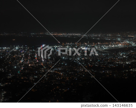 An elevated night view shows Cape Town lit grids, harbor lights, and ocean horizon, with high rises and waterfront, neon accents, ship lights, and long exposure look. 143146635